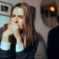 Smutna kobieta z rękami przy twarzy, siedząca z dala od mężczyzny. Czuć dystans po kłótni.