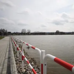 Spacerem nad zalewem wolbromskim, z czerwono-białą barierką i brukowaną ścieżką.