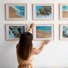 Frau arrangiert Bilder mit Strandmotiven. Tolle bilder anordnen ideen für eine sommerliche Wandgestaltung.