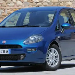 Una Fiat Punto blu brillante parcheggiata davanti a un muro di pietra.