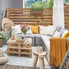 Przytulny taras w stylu boho z plecionymi meblami, poduszkami i paletowym stolikiem.