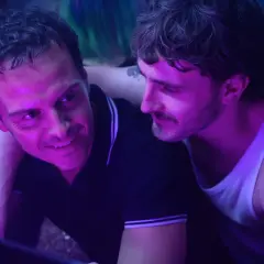 Dwóch mężczyzn w klubie, jeden z nich uśmiecha się do drugiego. To scena z filmu "Dobrzy nieznajomi", która zasługuje na recenzję.
