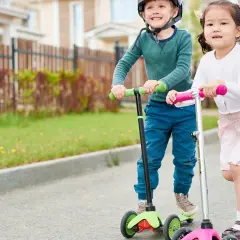 Dzieci na hulajnogach, chłopiec w kasku i dziewczynka, radośnie jadą ulicą. Od jakiego wieku hulajnoga? Już od najmłodszych lat!