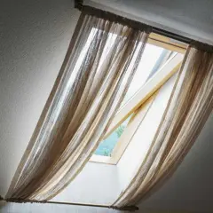 Voilage léger sur un montage store Velux ancien modèle, laissant passer la lumière du jour.