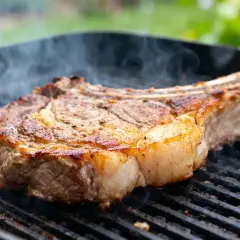 Une succulente basse côte de bœuf grésille sur un grill, dégageant une vapeur alléchante.