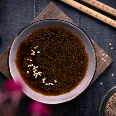 Schale mit Teriyaki-Sauce und Sesam, daneben Stäbchen und ein Glas Sesamsamen. Perfekt für dein Teriyaki Sauce Rezept!