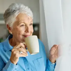 Uśmiechnięta starsza pani pije kawę, zastanawiając się, czego nie jeść przy wysokim cholesterolu.