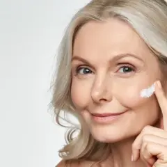 Eine Frau trägt Sonnencreme auf, um Falten vorzubeugen. Jeden Tag Sonnencreme gegen Falten schützt die Haut.