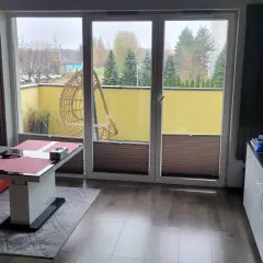 Wygodny salon z widokiem na atrium Radogoszcz. Na tarasie huśtawka i zieleń.