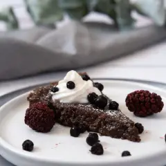 En bit vegansk kladdkaka med vispad grädde och bär.