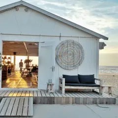 Biały domek plażowy z otwartymi drzwiami, widok na morze i wnętrze z ludźmi.