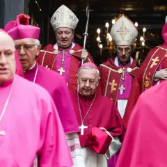 Biskupi w szatach w kolorze biskupi i fuksja, niosący krzyże i pastorały, idą w procesji.