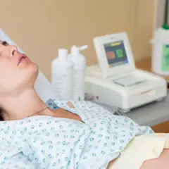 Kobieta w szpitalnym łóżku, monitor KTG, butelki z płynem. Badanie może wykluczyć obecność bakterii Streptococcus agalactiae.