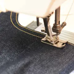 Close-up of a sewing machine stitching dark denim with yellow thread. Perfect sewing machine settings for denim are key for strong seams.