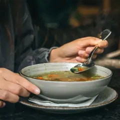 Gorący bulion warzywny na łyżce, idealny, gdy zastanawiasz się, co jeść przy gorączce.