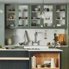 Stylish glass cabinet decor ideas in a modern kitchen with green cabinetry, showcasing ceramic bowls, plates, and glassware.