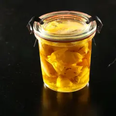 Un bocal en verre rempli d'ail confit dans de l'huile dorée. Les bienfaits de l'ail confit sont nombreux pour la santé.
