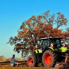 Ciągnik rolniczy pod jesiennym drzewem. Zastanawiasz się, ile kosztuje przekształcenie działki rolnej na budowlaną?
