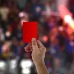 Dłoń trzyma czerwoną kartkę. Ile żółtych kartek może dostać zawodnik, zanim zobaczy tę?