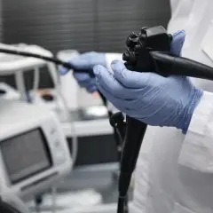 Lekarz w niebieskich rękawiczkach trzyma endoskop. Obok aparatury medycznej, która może wskazywać na zły wynik gastroskopii.