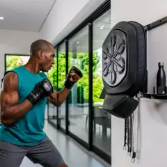 Man in a fighting stance throws a punch at a wall-mounted boxing reflex bag.