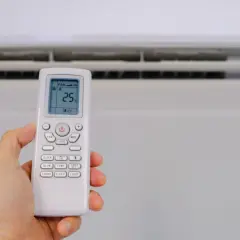 Mano sujetando control remoto de aire acondicionado, mostrando el símbolo deshumidificador aire acondicionado en pantalla.