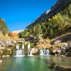 Cascada en un valle montañoso con árboles otoñales. Un lugar perfecto para rutas de senderismo inolvidables.