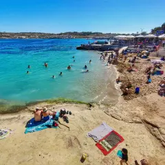 Słoneczna plaża z turkusową wodą, na której kąpią się ludzie, a na piasku odpoczywają plażowicze.