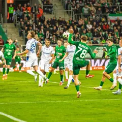 Piłkarze Lecha Poznań w białych strojach i Śląska Wrocław w zielonych grają w piłkę nożną na boisku.