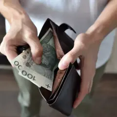 Ręce wkładają polskie banknoty 100 zł do portfela. Czy to wystarczy na świadczenia z MOPS dla niepełnosprawnych?