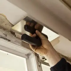 Ręka z kielnią wygładza tynk wokół framugi okiennej.