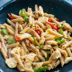 Makaron penne z kurczakiem i papryką w czarnej patelni.