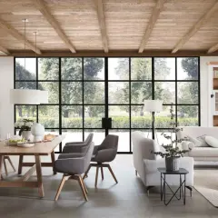 Geräumiges Esszimmer mit Holzbalkendecke im Bauernhaus Stil, Holztisch, grauen Stühlen und großer Fensterfront mit Blick ins Grüne.
