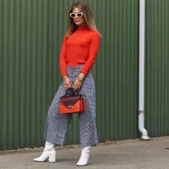 Modna kobieta w pomarańczowym golfie i kraciastych jeansowych kulotach, białych kozakach i torebce. Stylowe jeansowe kuloty stylizacje.