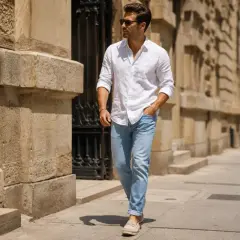 Mężczyzna w białej koszuli i jasnych jeansach stylizacjach spaceruje po ulicy.