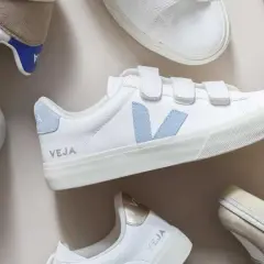 Plusieurs baskets Veja blanches, certaines avec des touches de couleur, sont disposées sur un fond clair. Idéal pour apprendre comment nettoyer des baskets.