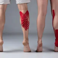 Dwie nogi z czerwonymi taśmami do **taping limfatyczny** na łydkach. Jedna noga ma skomplikowany wzór, druga prostsze paski.