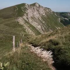 Sentier rocailleux bordé de piquets en bois, menant vers un sommet escarpé. Une invitation à la grande traversée du Jura 7 jours.