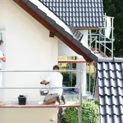 Dwóch mężczyzn na rusztowaniu maluje białą elewację. Sprawdzają tynk silikonowy cena za m2 robocizny.