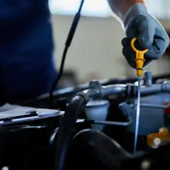 Mechanik w rękawiczce sprawdza poziom oleju za pomocą żółtej miarki. To ważny element kontroli silnika, podobnie jak sprawna odma olejowa.
