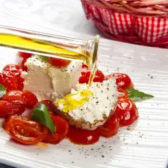 Un piatto di pomodorini confit con robiola, perfetto per un pasto leggero e nutriente in gravidanza. Olio d'oliva versato su una fetta di pane con formaggio.