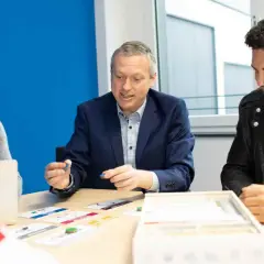 Ein Mann erklärt jungen Leuten beim dualen Studium Marketing Berlin ein Spiel.