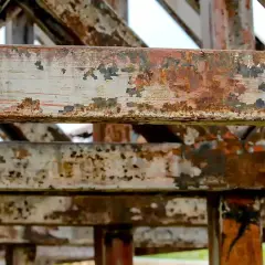 Metalowe belki konstrukcji zniszczone przez czas. Widoczna łuszcząca się farba i rdza, świadczące o postępującej korozji fizycznej.