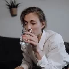 Kobieta w białej koszuli pije wodę ze szklanki.