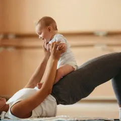 Une mère fait des exercices pour renforcer son périnée après accouchement, soulevant son bébé joyeux.