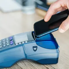 Dłoń zbliża smartfon do terminala płatniczego, realizując szybki booking paypo.
