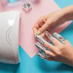 Rimozione smalto semipermanente: unghie avvolte in stagnola, lampada UV e glitter. Attenzione, il semipermanente rovina le unghie se non rimosso correttamente.
