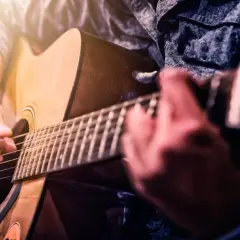 Ręce grające na gitarze akustycznej. Dowiedz się, jak samemu nauczyć się grać na gitarze, ćwicząc akordy i rytm.