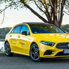Żółty Mercedes A250 z czarnym dachem i felgami, zaparkowany nad jeziorem.