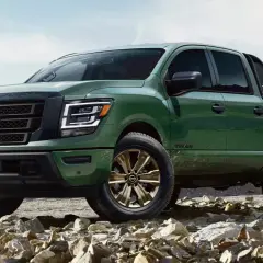Zielony Nissan Titan z brązowymi felgami na kamienistym podłożu, gotowy na przygodę w górach.
